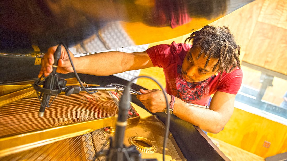A student reaches under the lid of a piano with a cable attached to sound equipment