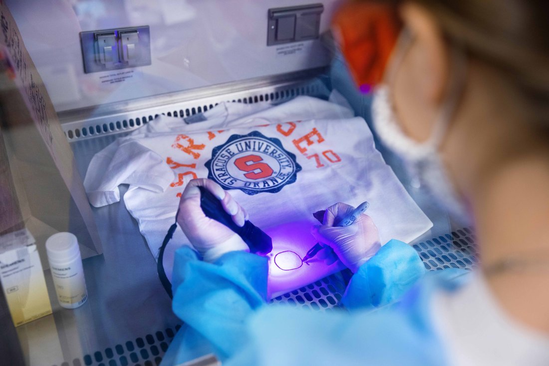 Woman in lab coat examining t-shirt for evidence