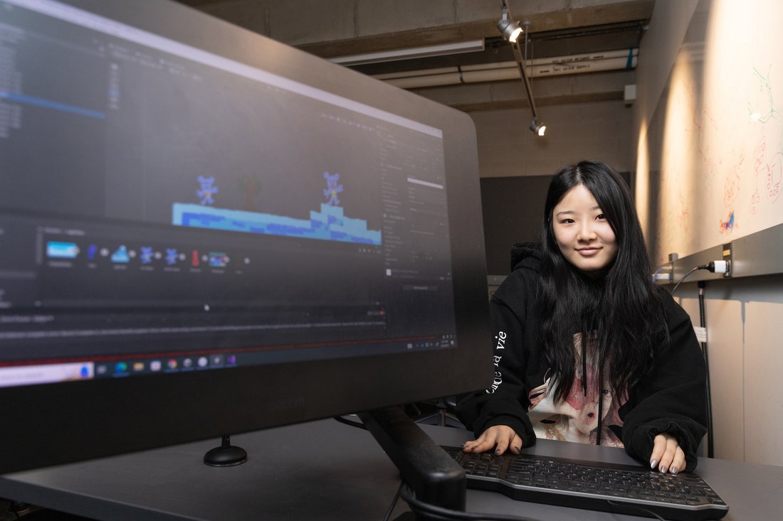 A student sits next to a computer screen that displays a computer game