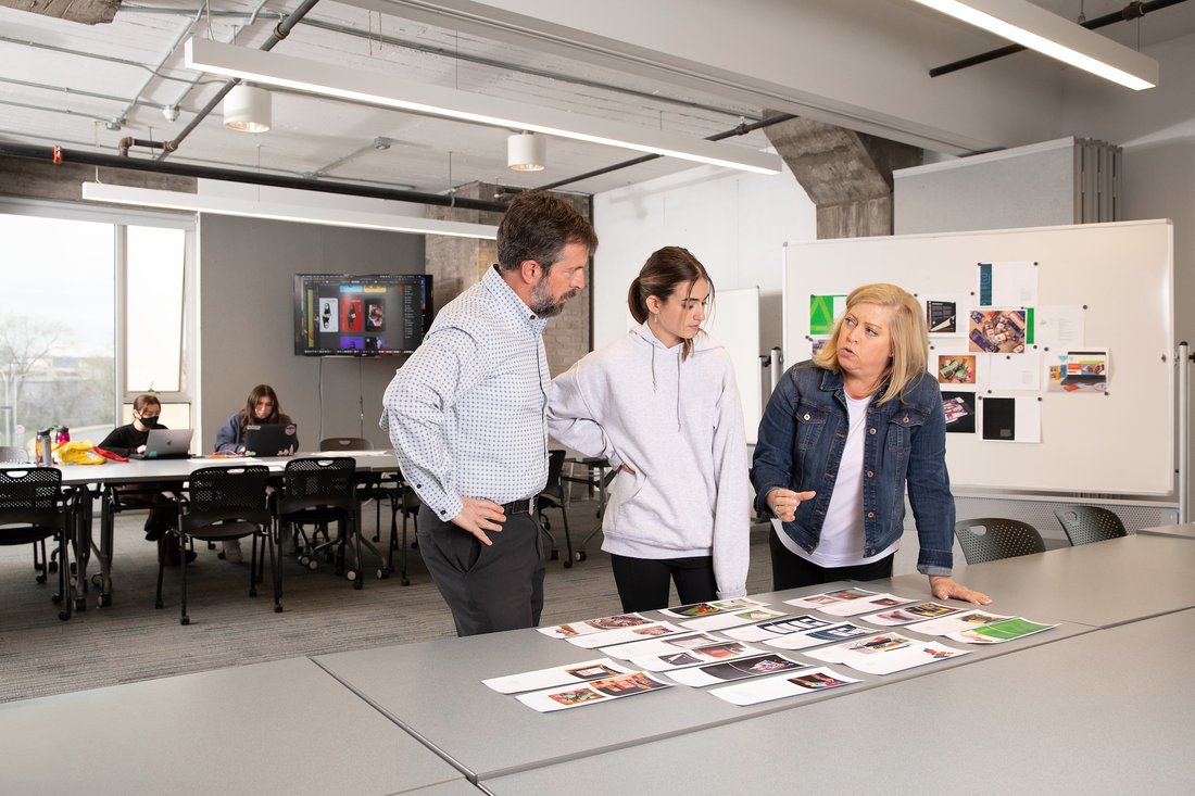 Two teachers and a student look at prints of images on a table in a studio