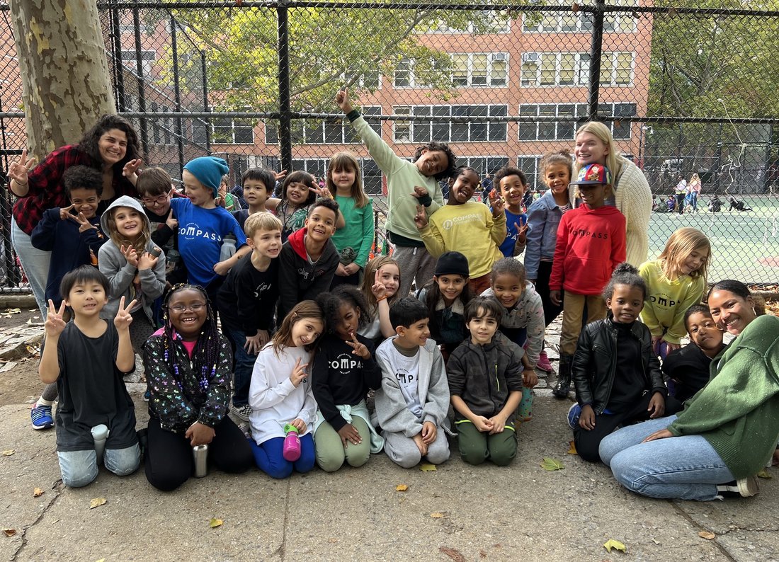 Three student teachers pose with a group of elementary school students outside of a school in brooklyn