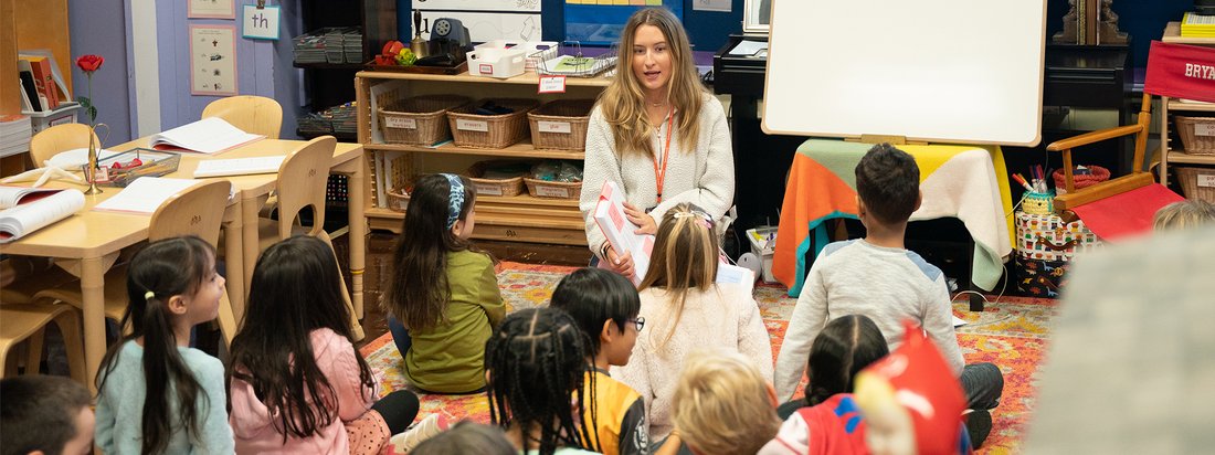 Children sitting in classroom listening to teacher talk.
