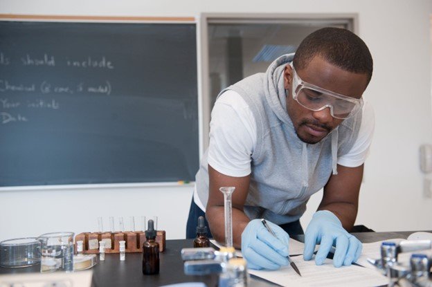 Person wearing rubber gloves and safeth glasses writing in a lab