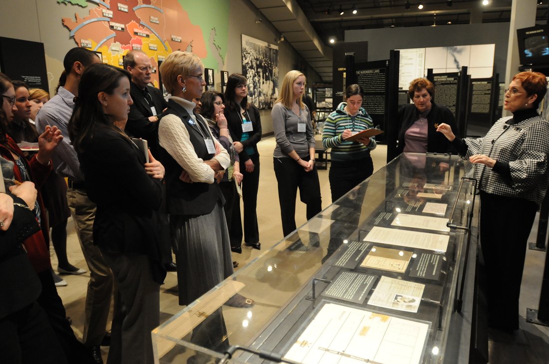 a group of student watches a docent describe items in a display case at the holocaust museum houston